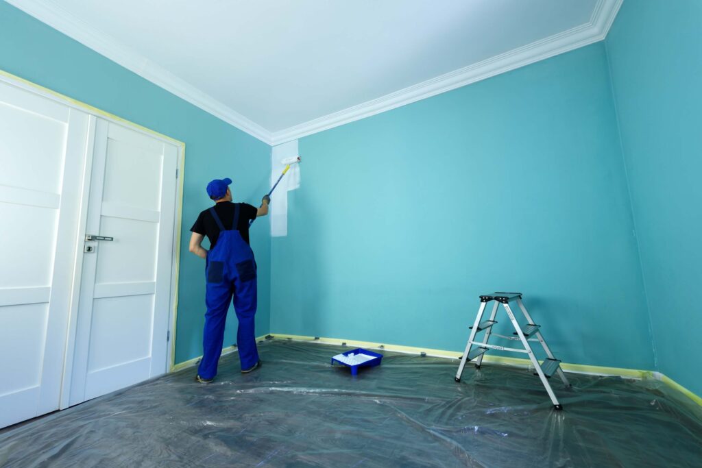 A painter applies a semi-gloss finish to an interior wall using a roller.
